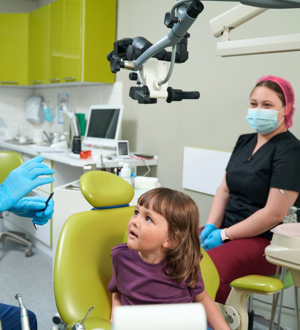 Pediatric dentist conversing with little girl before dental examination